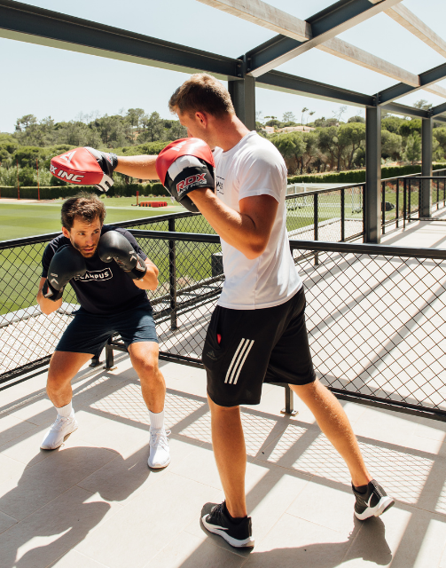 Dois homens com equipamento de boxe a praticar socos numa área de treino no The Campus.