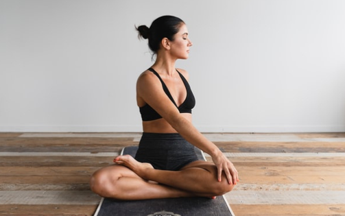 Uma mulher com um soutien desportivo preto e calções senta-se num tapete de yoga no The Campus, pronta para o seu treino.